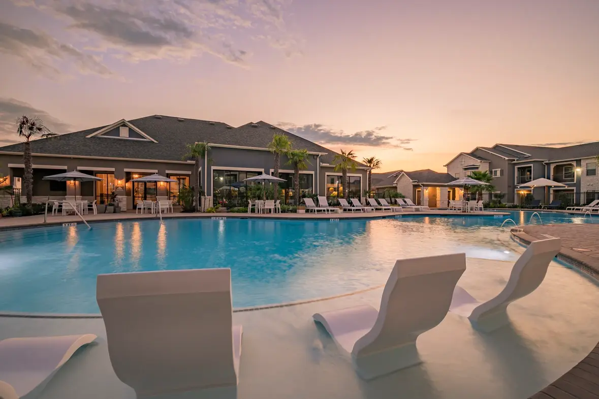 An apartment community pool at sunset with poolside chairs.