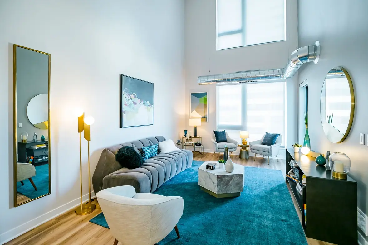 A furnished apartment living room featuring tall ceilings, a blue carpet, and gray couch.