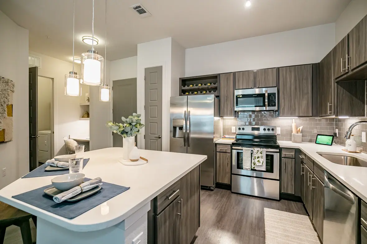 A kitchen in an apartment with dark cabinets, white countertops, and stainless steel appliances.