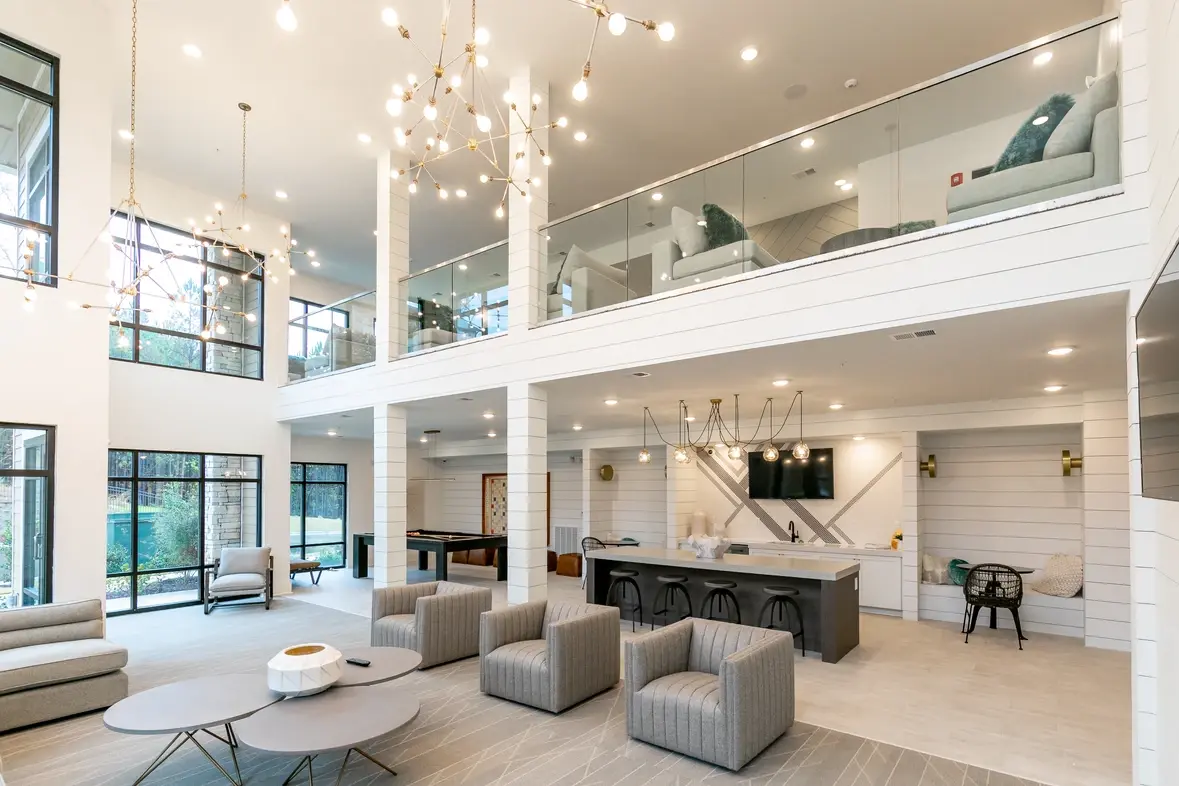 An apartment community clubhouse with tall ceilings, gray furniture, and beautiful lighting.