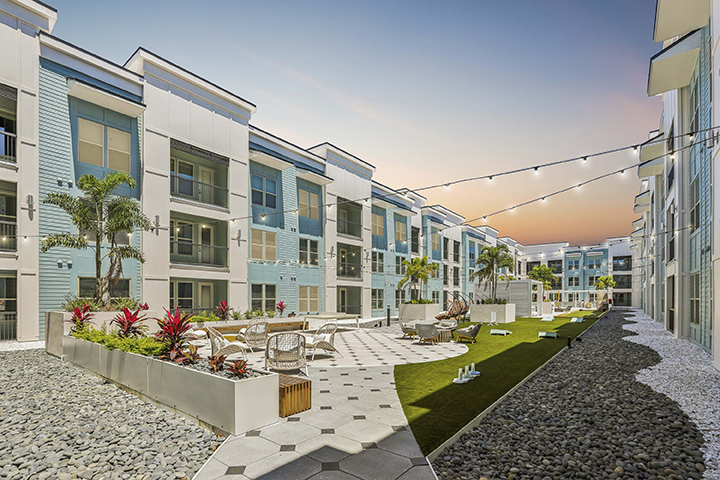 An apartment community outdoor patio at sunset with string lights and palm trees.