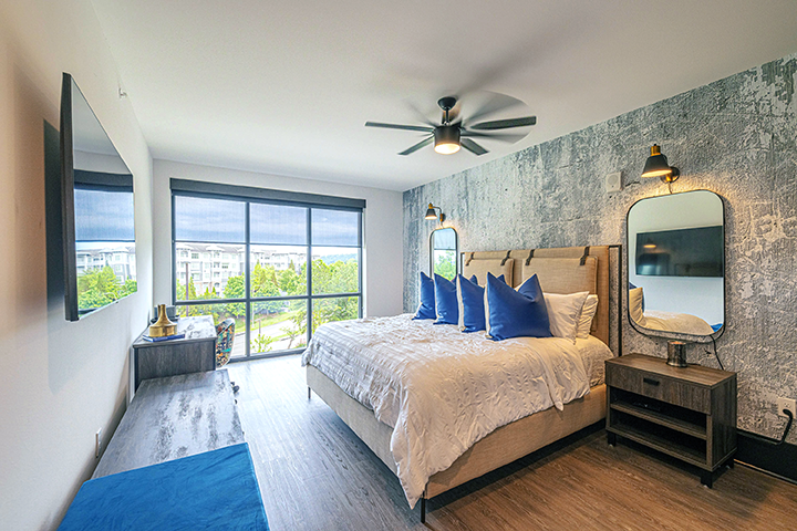Furnished apartment bedroom with a window view outside to an apartment community.