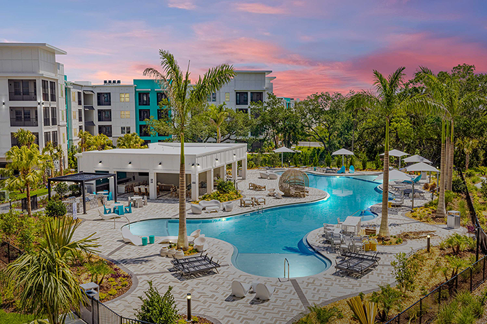 An extended view of an apartment community and large pool at sunset.