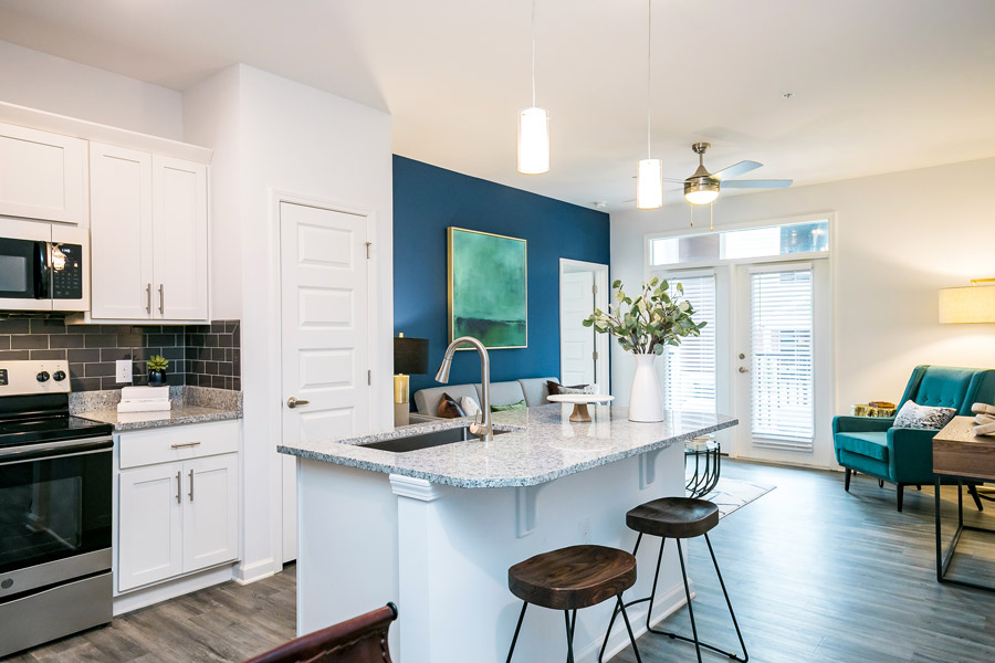 Apartment kitchen with white cabinets, a stainless oven, and a white island with stools, opening onto the living area.