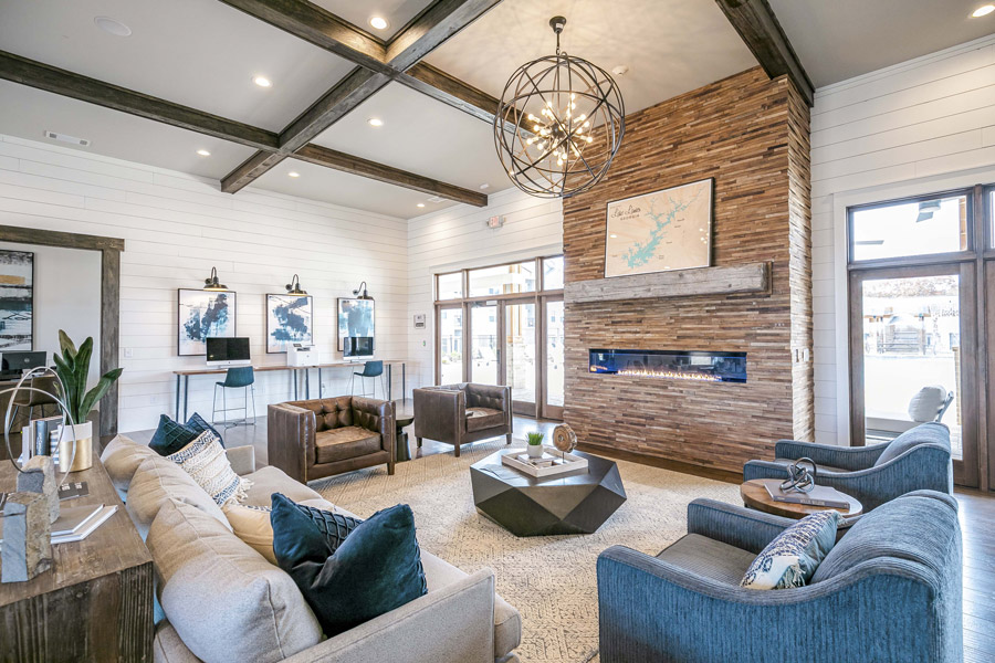 Living room with a vaulted beamed ceiling, ceiling fan, built-in shelving, and blue upholstered seating beneath tall windows.