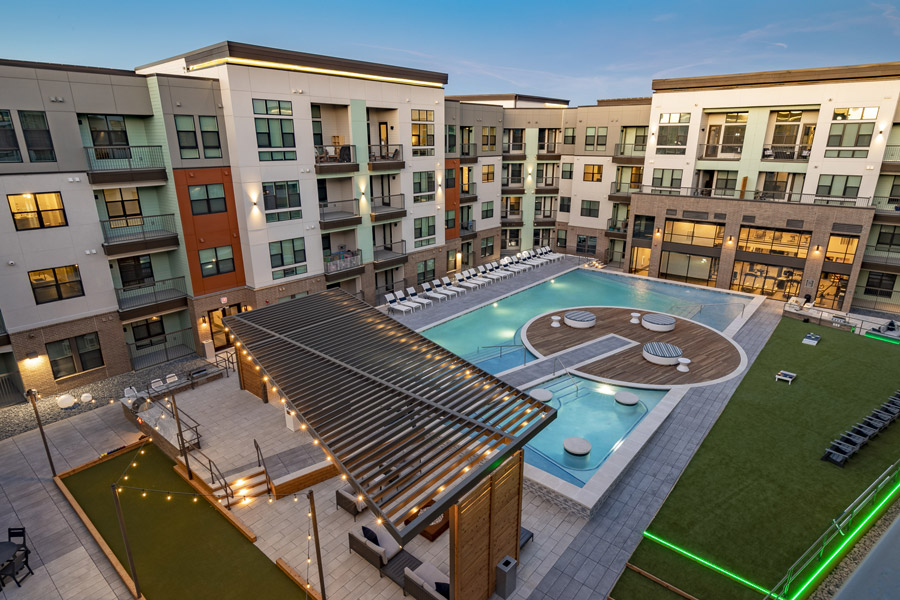 Aerial view of a courtyard pool at the center of a low-rise apartment complex, with a lawn alongside it.