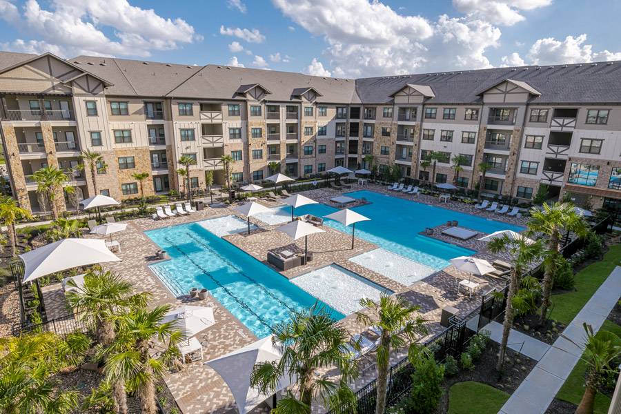 Elevated view of a large resort-style pool surrounded by an apartment complex and landscaping.
