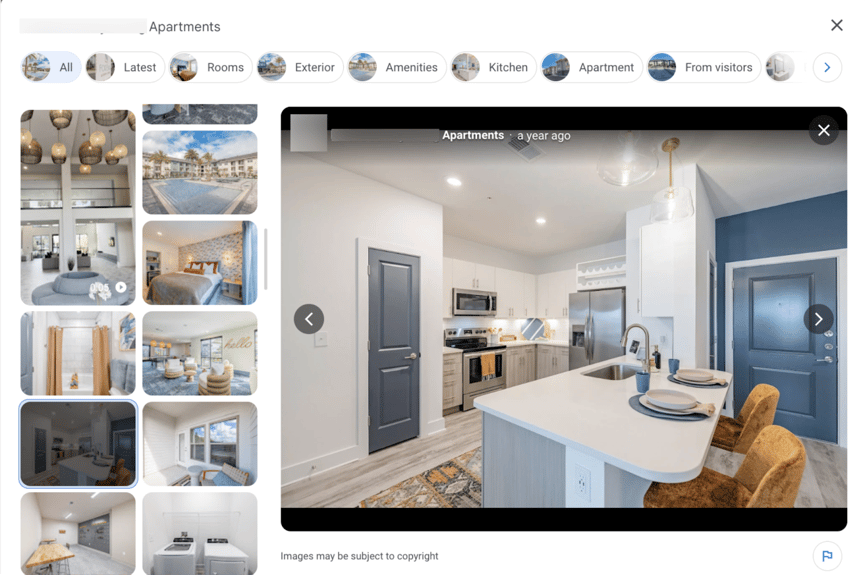 A screenshot of a Google Business Profile phot gallery featuring a modern apartment kitchen with white cabinets, stainless steel appliances, and a navy accent door. A large island features bar seating with gold velvet chairs and place settings. Pendant lights and wood-style flooring complete the bright, contemporary design.