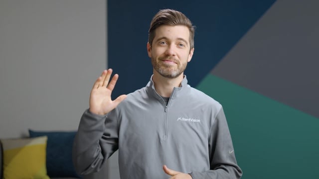 Smiling RentVision team member in a navy branded quarter-zip standing in front of a white brick wall in a bright office.