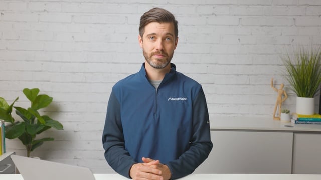 Smiling RentVision team member in a navy branded quarter-zip standing in front of a white brick wall in a bright office.