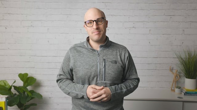 Smiling RentVision team member in a quarter-zip standing in front of a white brick wall in a bright office.