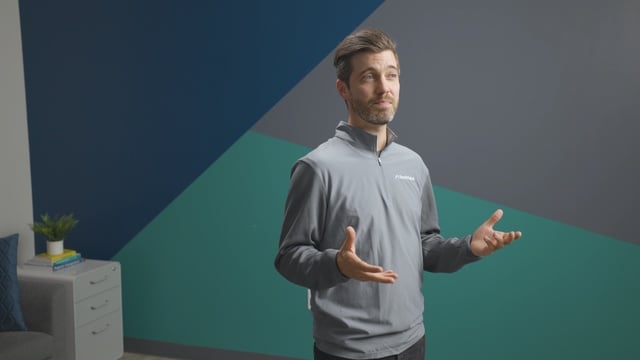 Smiling RentVision team member in a navy branded quarter-zip standing in front of a white brick wall in a bright office.