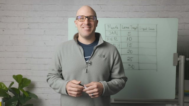 Smiling RentVision team member in a navy branded quarter-zip standing in front of a white brick wall in a bright office.
