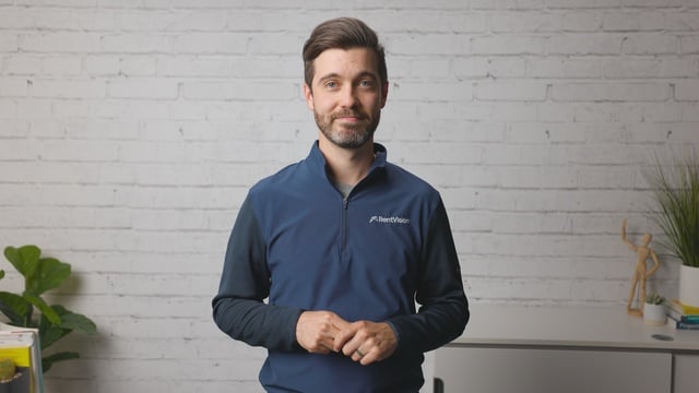 Smiling RentVision team member in a navy branded quarter-zip standing in front of a white brick wall in a bright office.