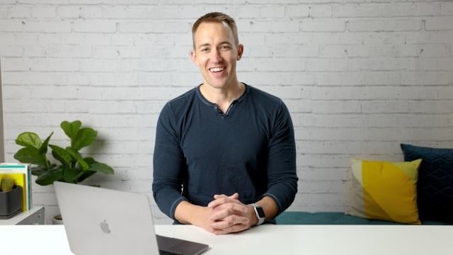 Smiling RentVision team member sitting in front of a white brick wall in a bright office.