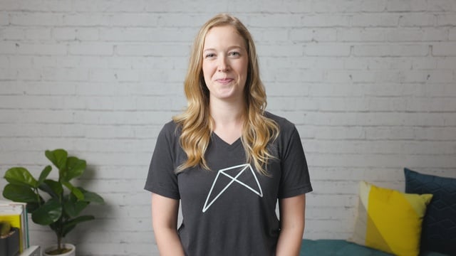 Smiling RentVision team member in a gray branded t-shirt standing in front of a white brick wall in a bright office.