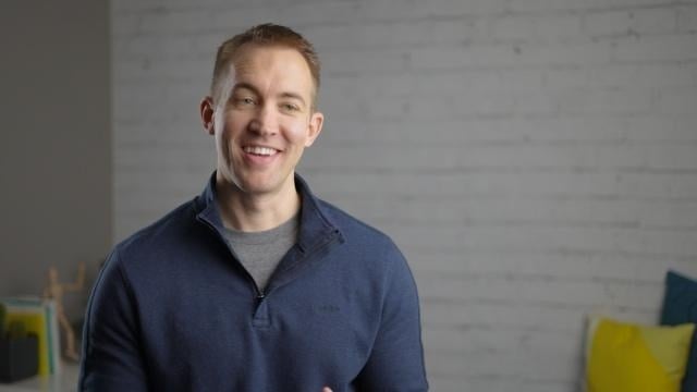 Smiling RentVision team member in a navy branded quarter-zip standing in front of a white brick wall in a bright office.