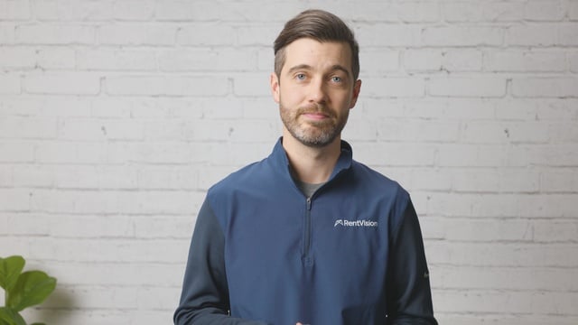 Smiling RentVision team member in a navy branded quarter-zip standing in front of a white brick wall in a bright office.
