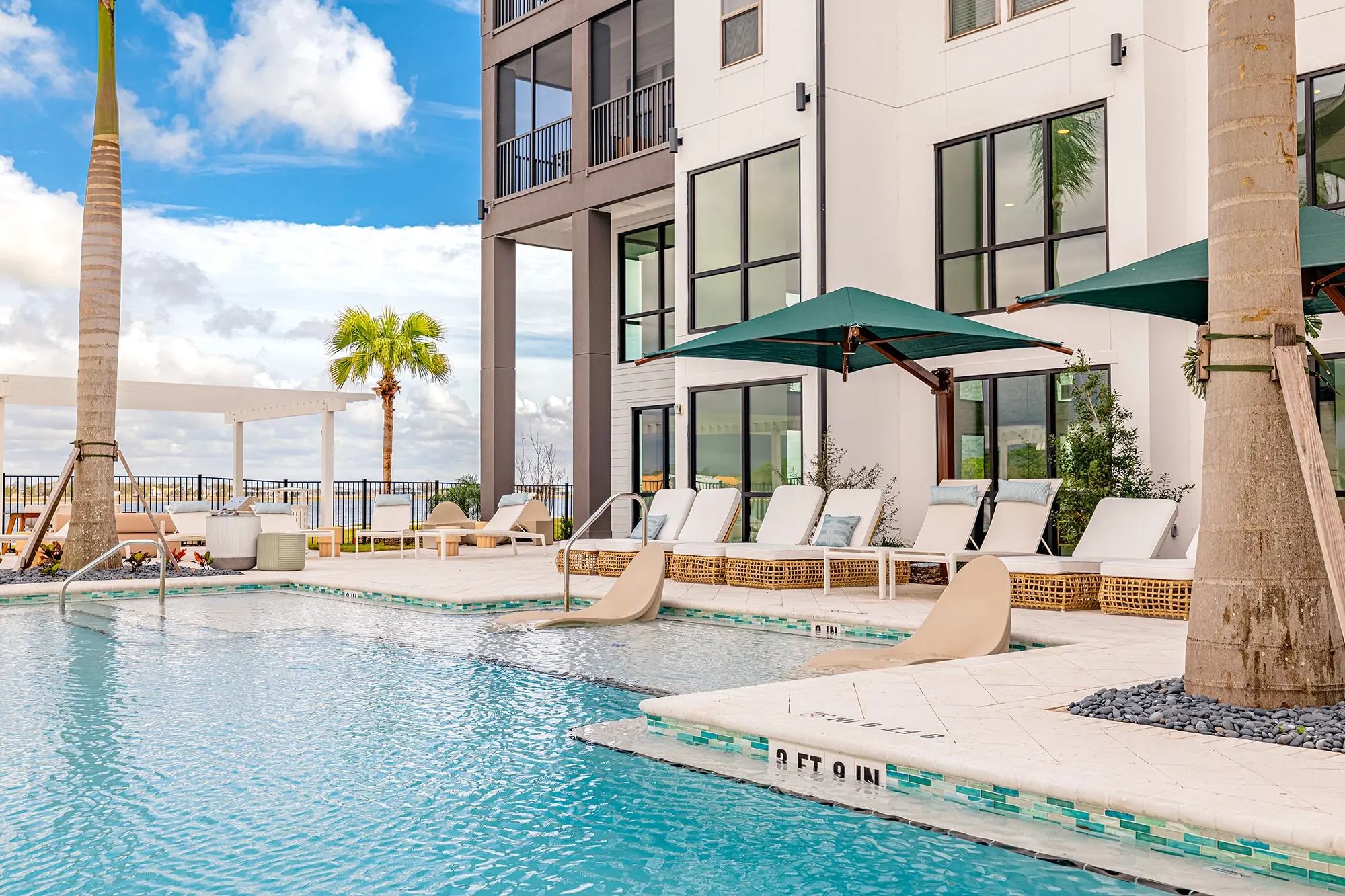 After: the same pool deck with bright blue sky, clear water, and green umbrellas.