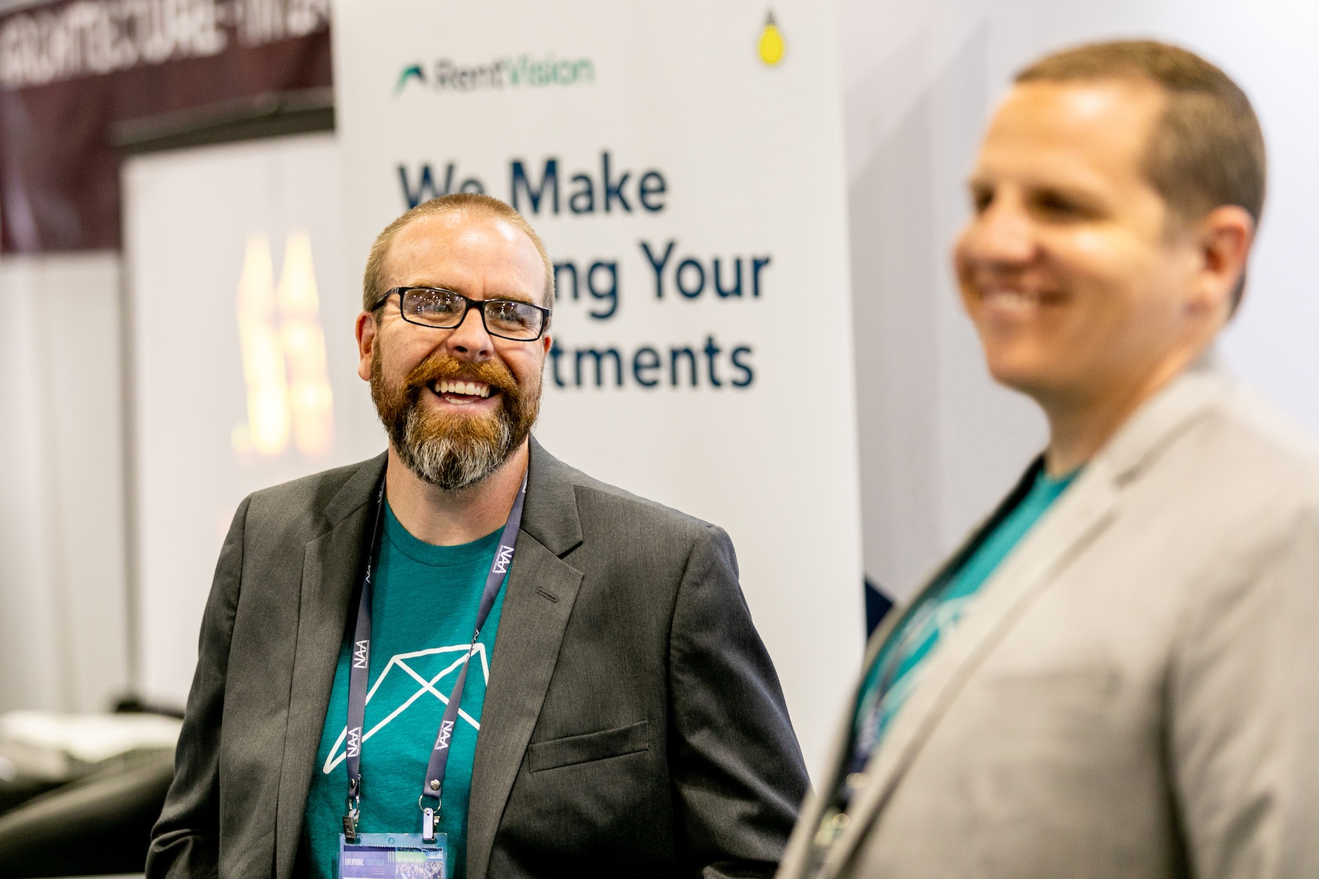 Two men wearing t-shirts with RentVision logo smiling in trade show booth.